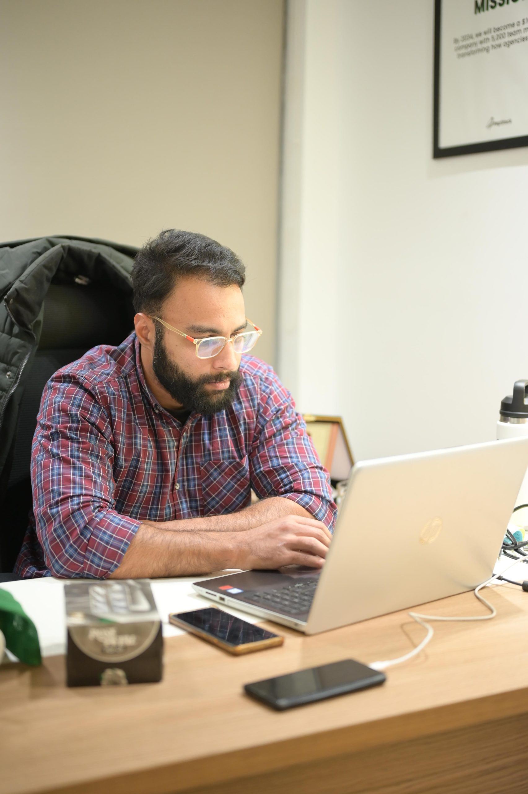 Man working on a laptop in an office setting, focused on digital tasks, with a smartphone and a coffee cup nearby, illustrating the importance of SEO strategies for businesses.
